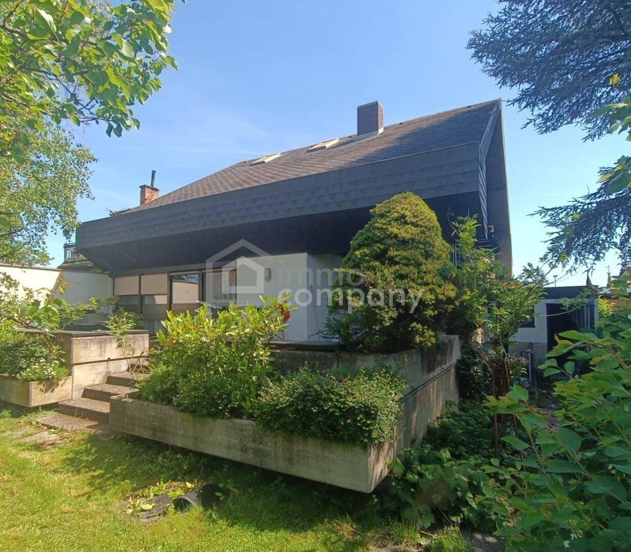 Seitenansicht des Hauses mit Terrassen und üppiger Bepflanzung im Gartenbereich.