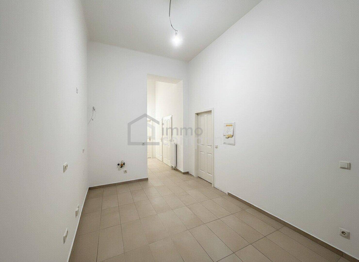 Leerer Raum mit Fliesenboden und Anschlüssen, bereit für die Kücheninstallation.
