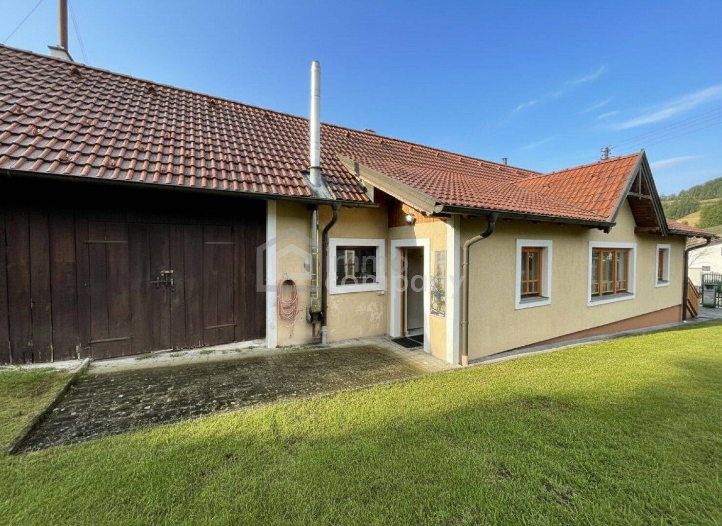 Ländliches Haus mit gelber Fassade, roten Ziegeldächern und einem großen grünen Rasenbereich.