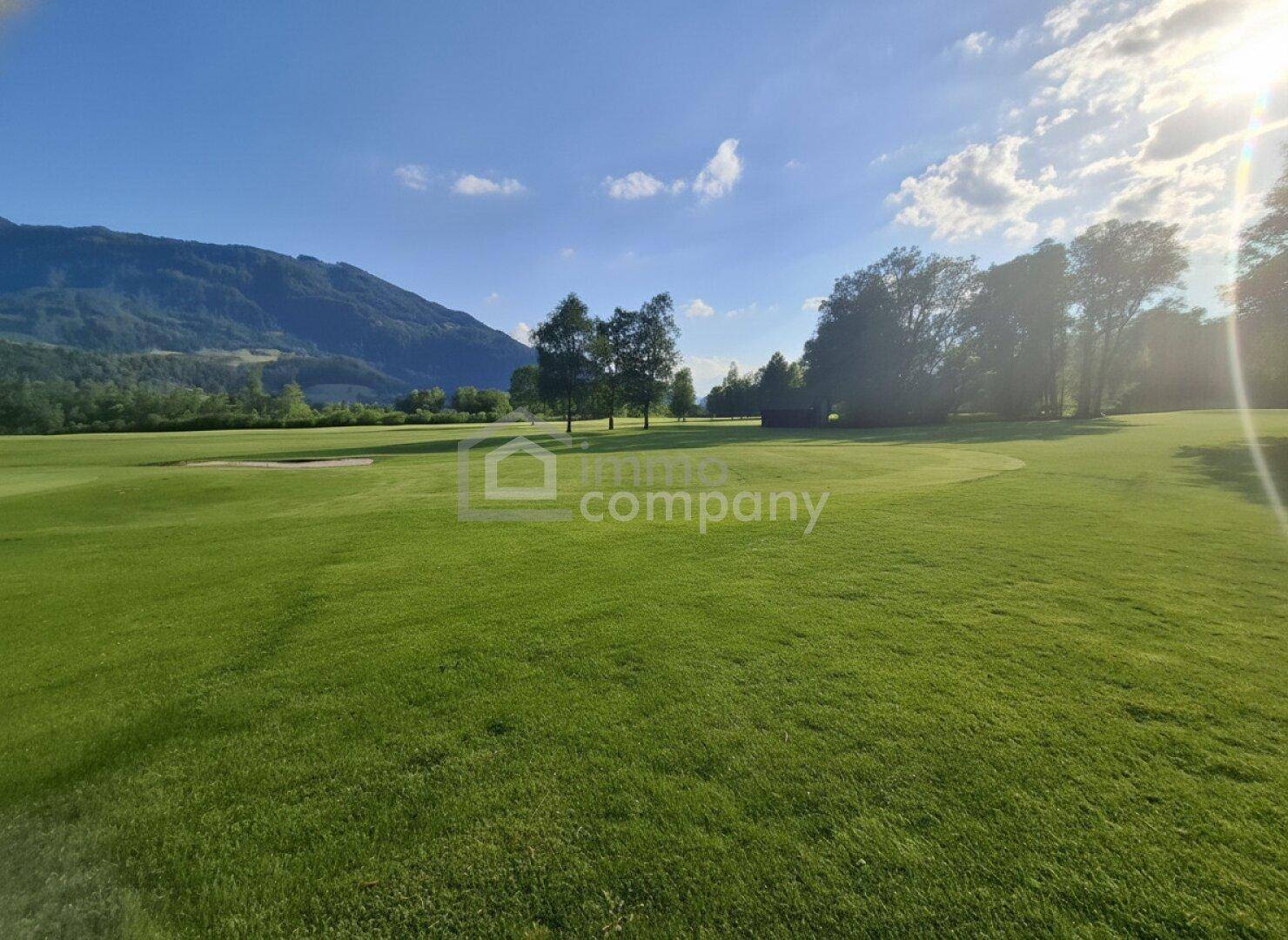 Sonnendurchfluteter Golfplatz mit weiten Rasenflächen und einer beeindruckenden Berglandschaft.