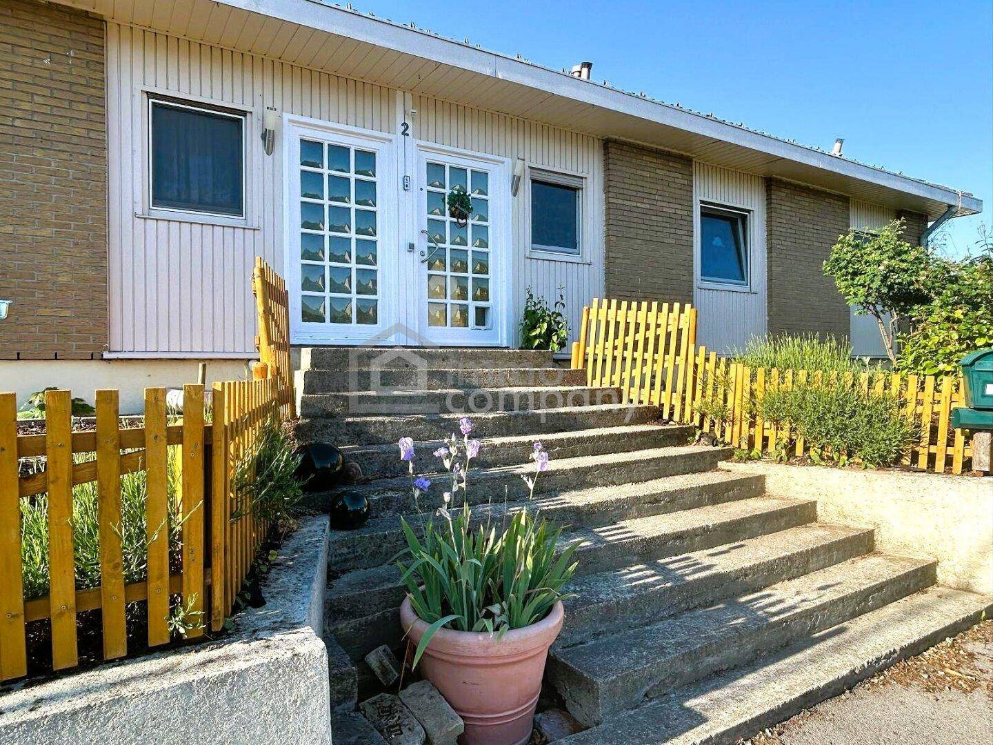 Eingangsbereich des Hauses mit Betontreppe, gelbem Zaun und doppelter Eingangstür.