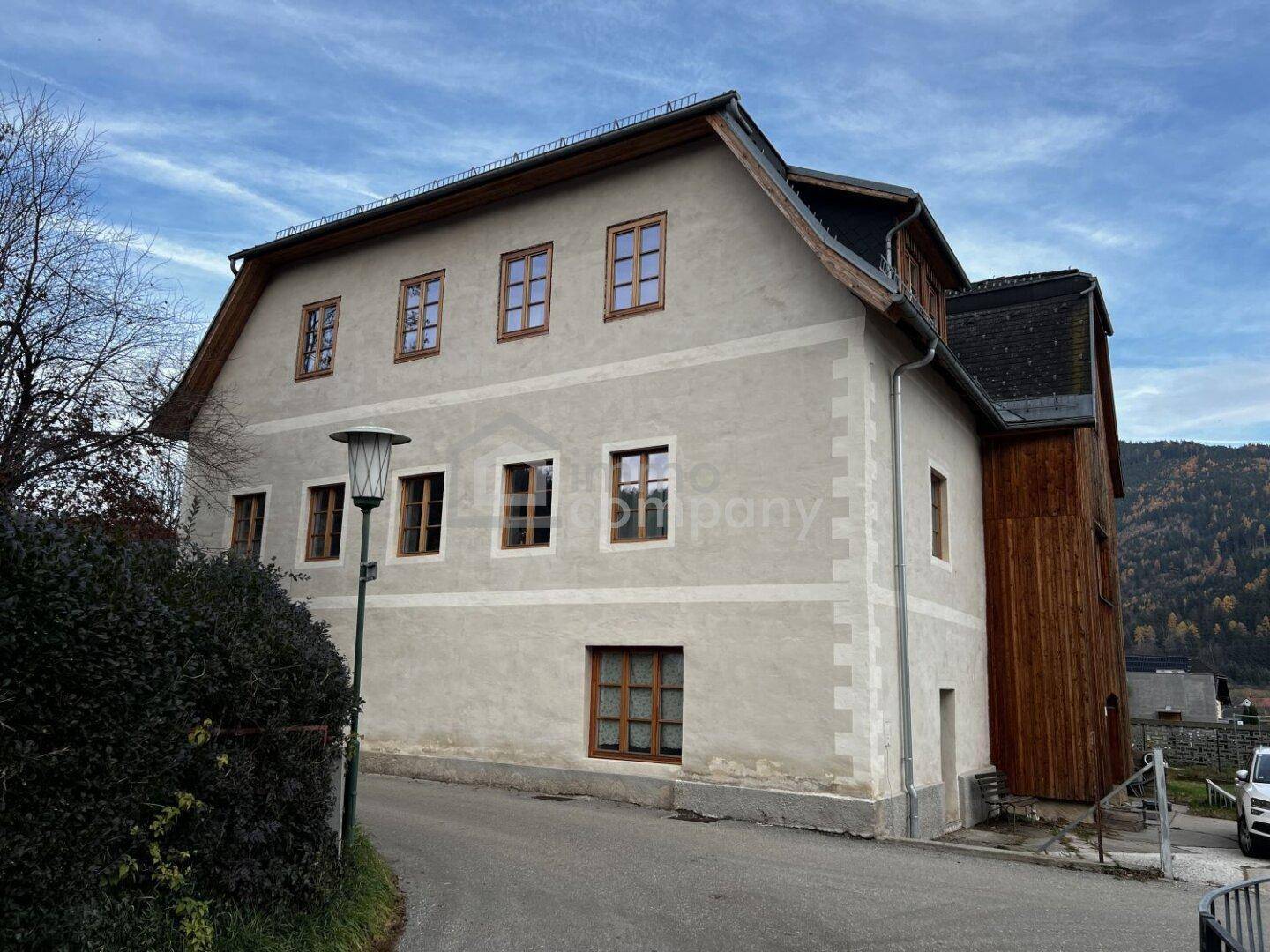 Seitenansicht des historischen Gebäudes mit traditionellen Fenstern und ländlicher Umgebung.