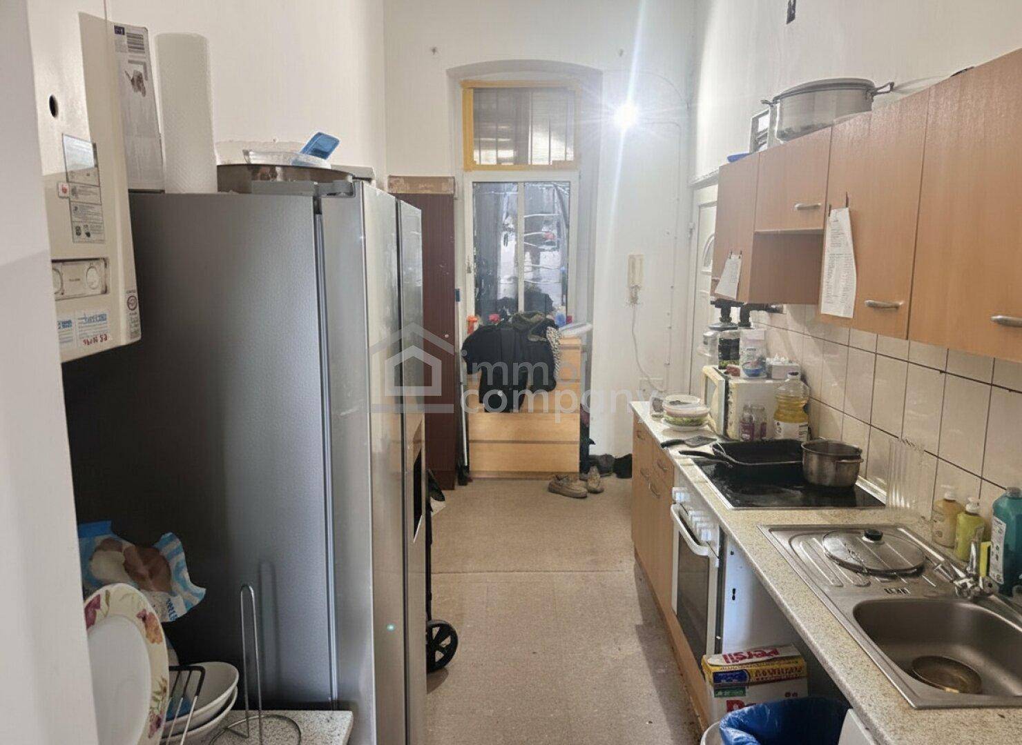 Schmale Küche mit älteren Einbauschränken, Kühlschrank und Herd.