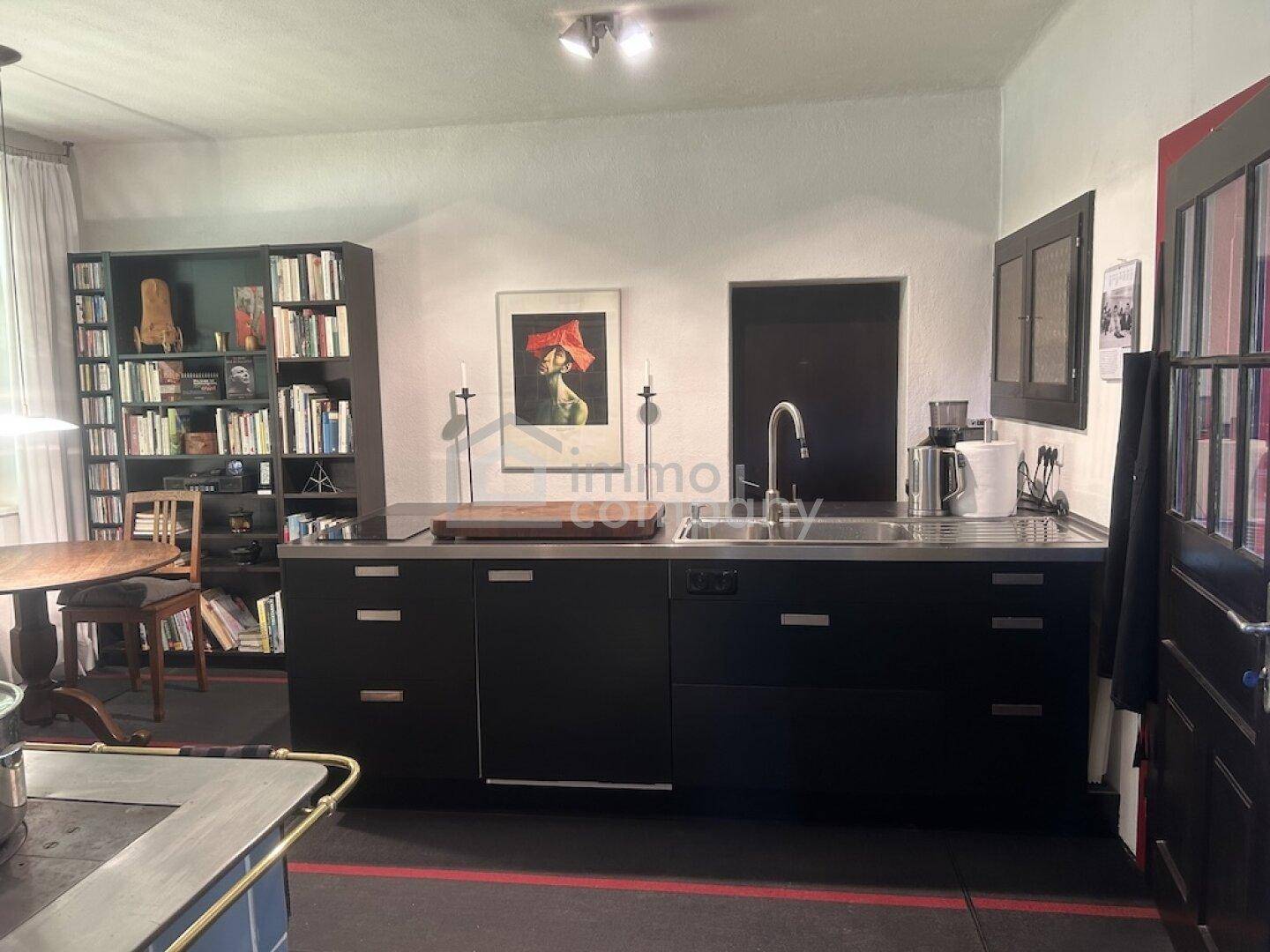 Moderne schwarze Einbauküche mit Spüle, Arbeitsplatte und Bücherregal im Hintergrund.