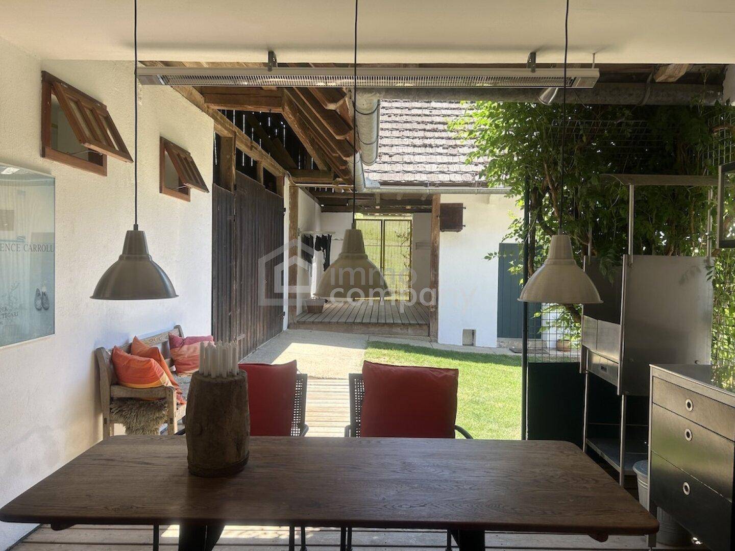 Überdachter Essbereich im Freien mit Holztisch, Stühlen und Blick auf den Garten.