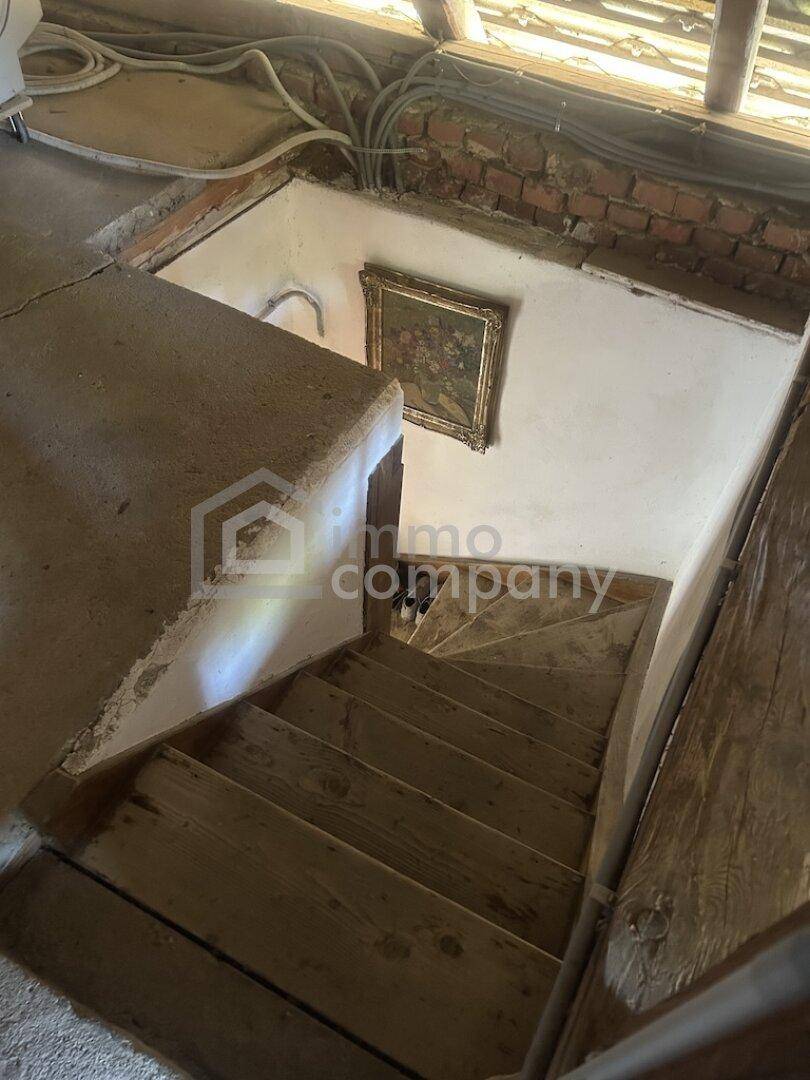 Rustikale Holztreppe führt hinunter in einen älteren Bereich mit einem kleinen Gemälde an der Wand.