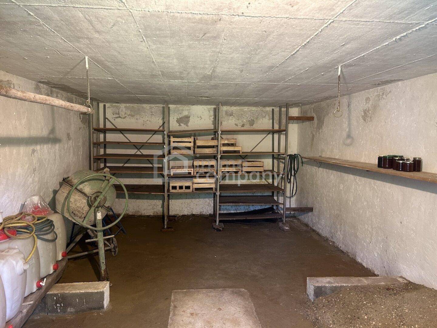 Geräumiger Kellerraum mit Betonwänden, Regalen und einem Zementmischer.