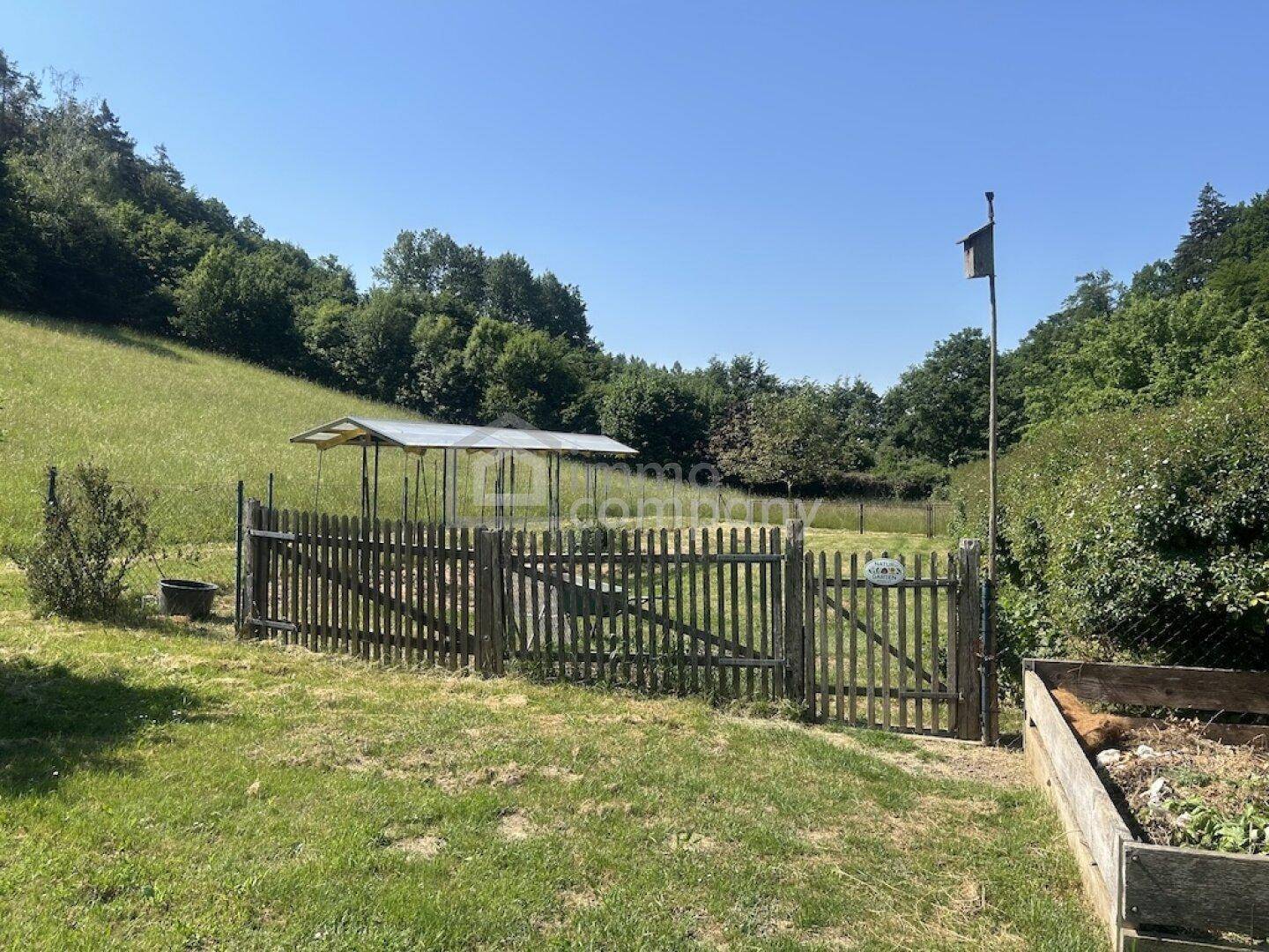 Eingezäunter Gartenbereich mit Hochbeeten, einem kleinen Unterstand und viel Grün.