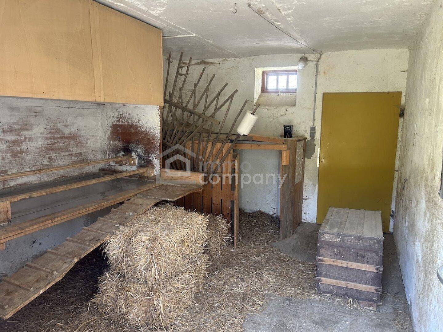 Rustikaler Innenraum, möglicherweise ein Stall, mit Heuballen und Holzkonstruktionen.