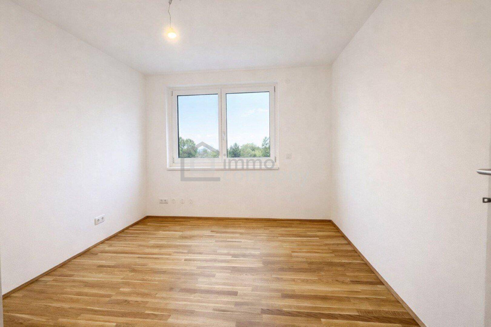 Leeres Zimmer mit hellem Parkettboden und großem Fenster, bietet vielseitige Nutzungsmöglichkeiten.
