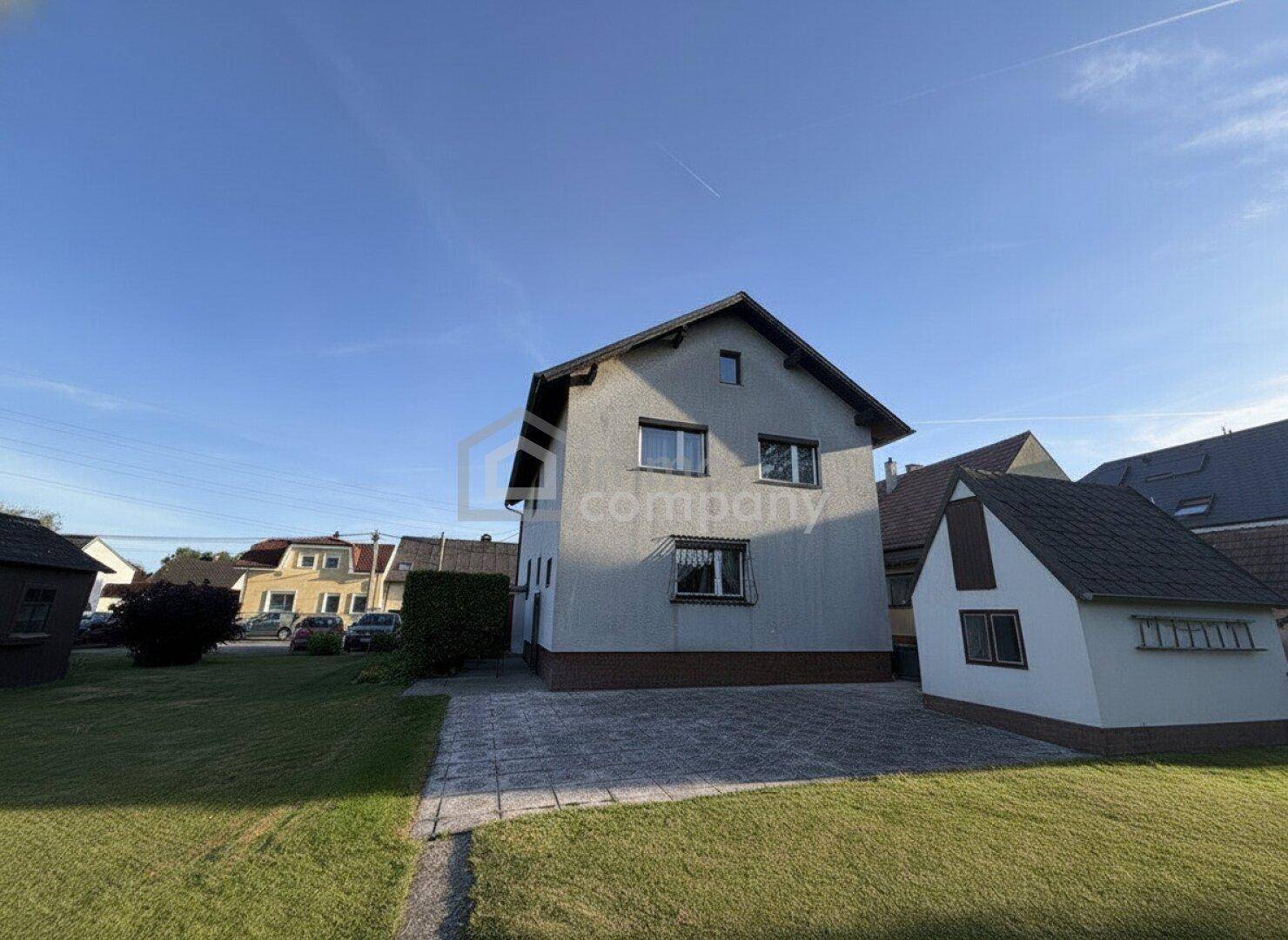 Einfamilienhaus mit gepflasterter Auffahrt und Rasenfläche, umgeben von weiteren Wohnhäusern.