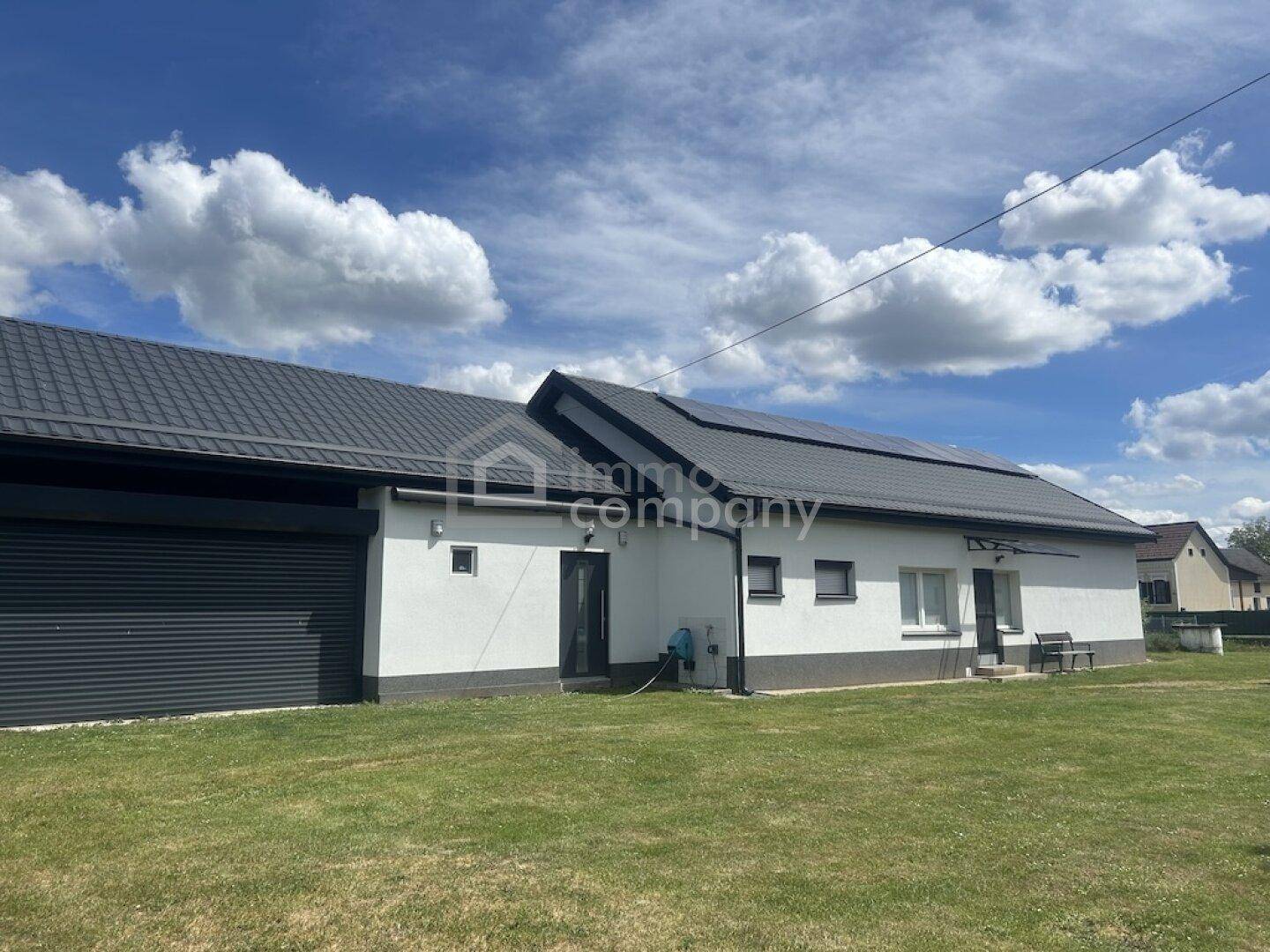 Ansicht des Hauses mit integrierter Garage, Solarpaneelen und gepflegtem Rasen unter blauem Himmel.