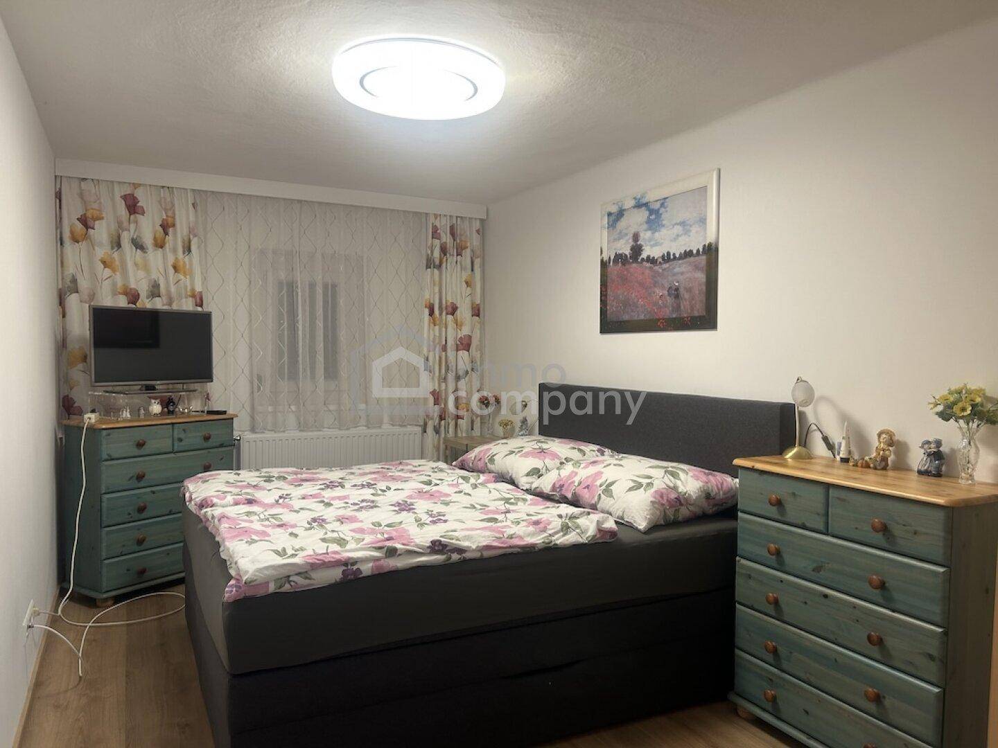 Gemütliches Schlafzimmer mit Doppelbett, Holzboden und bunten Vorhängen, gut beleuchtet.
