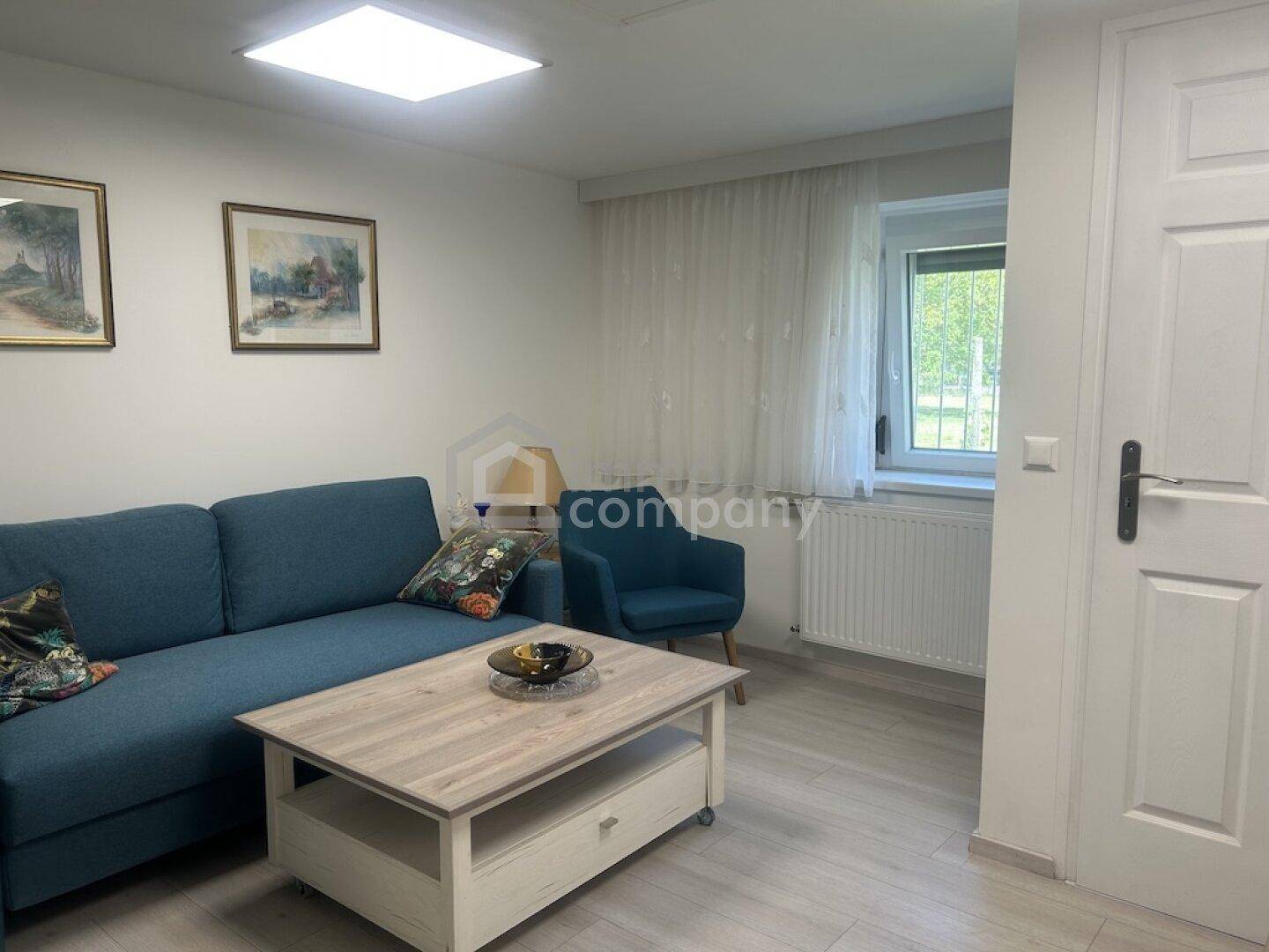 Modern eingerichtetes Wohnzimmer mit blauem Sofa, Couchtisch und hellem Fliesenboden.