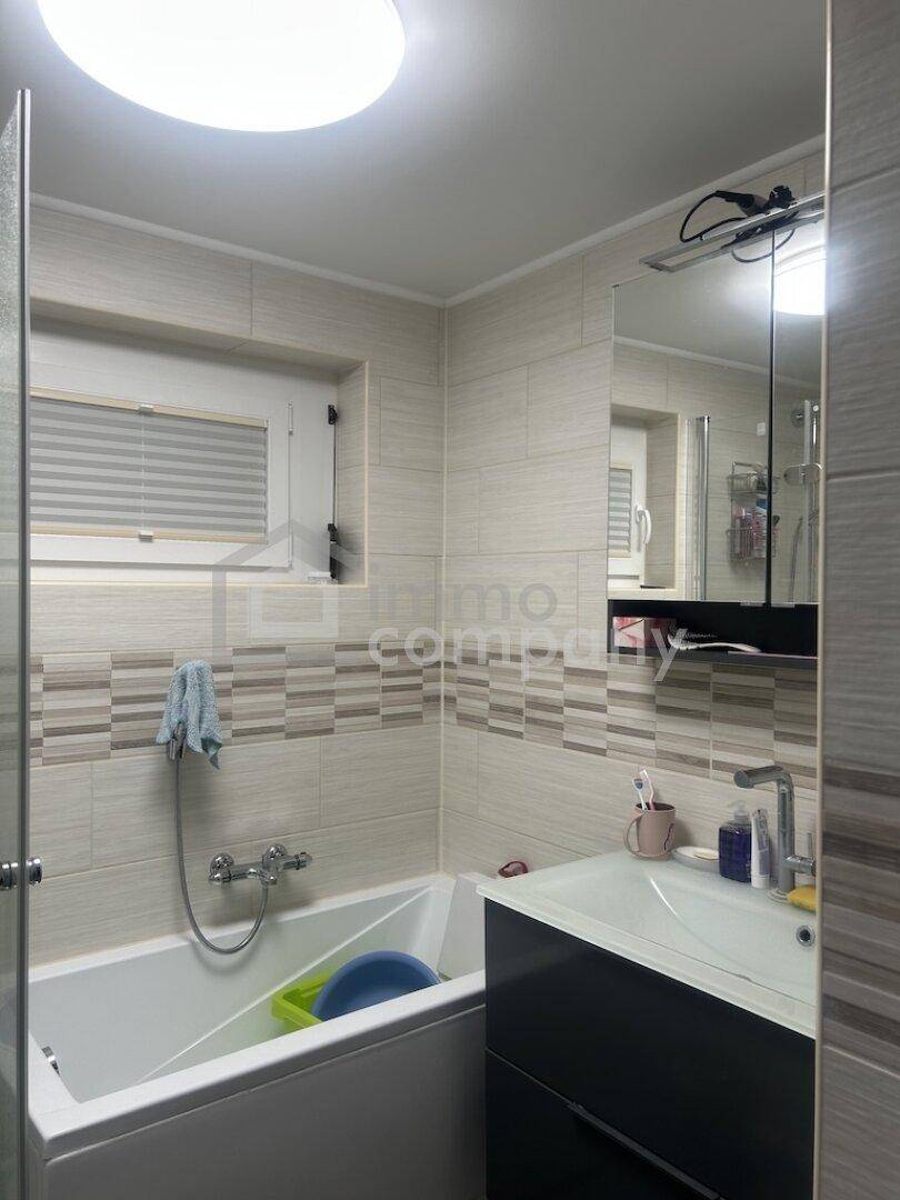 Modern gefliestes Badezimmer mit Badewanne, Waschbecken und Spiegelschrank, mit Fenster.