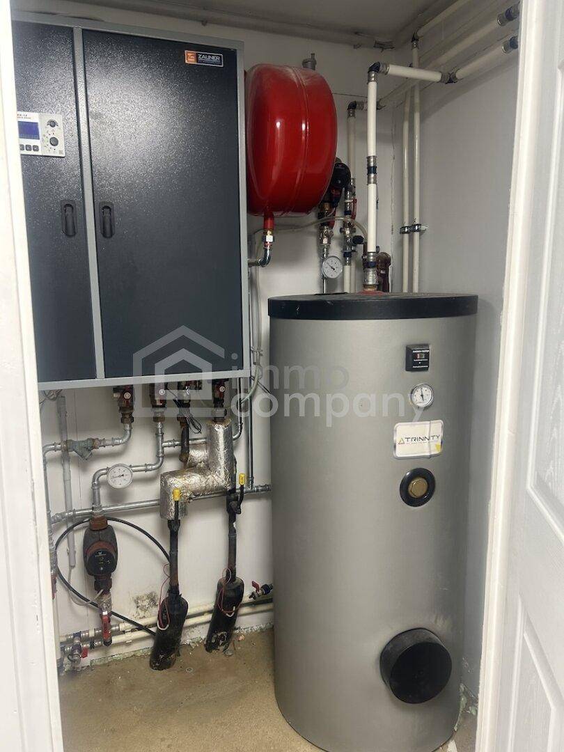 Technikraum mit Heizungsanlage, Warmwasserspeicher und sichtbaren Rohrleitungen, funktional gestaltet.