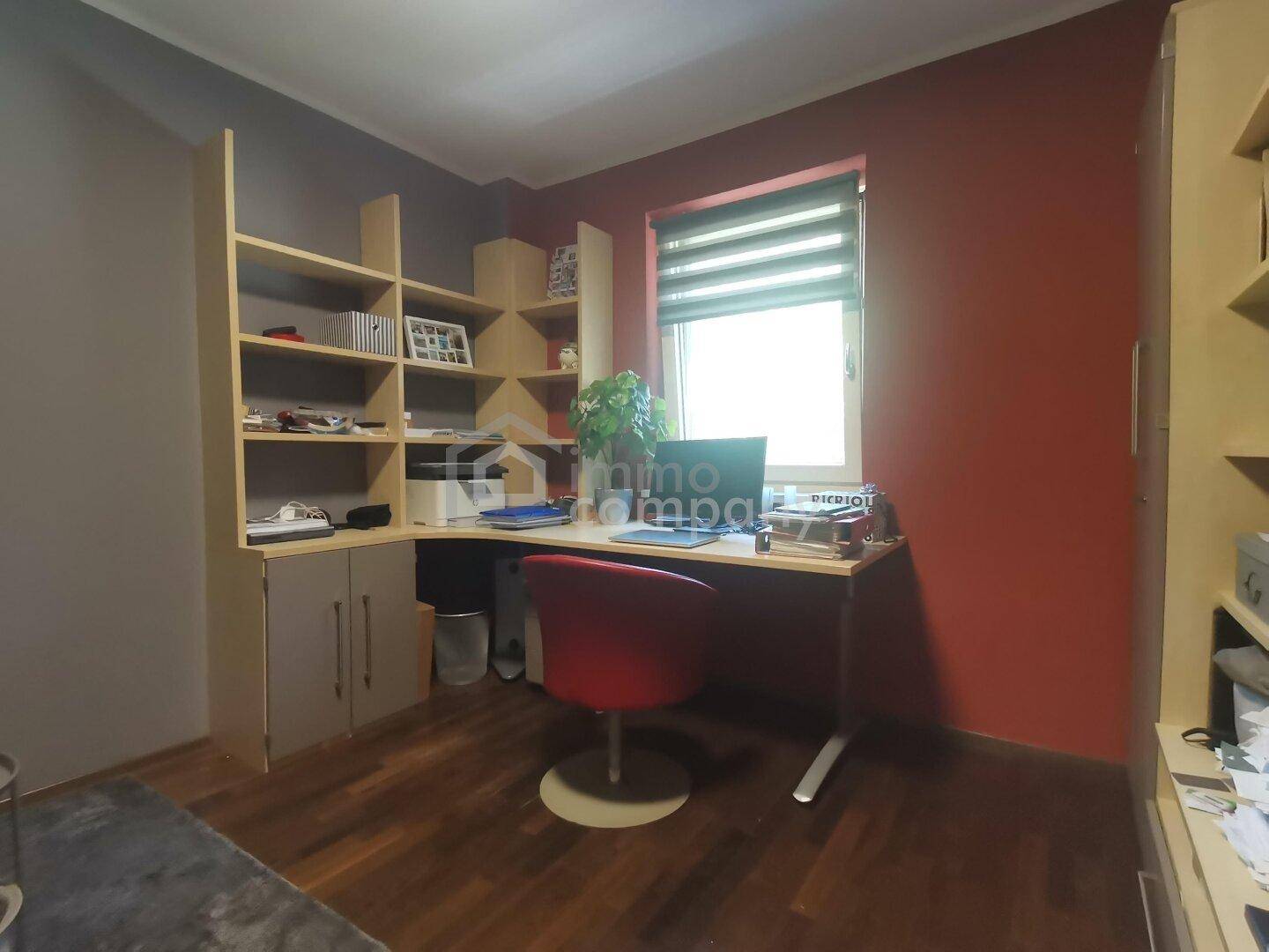 Funktionales Arbeitszimmer mit Holzboden, Schreibtisch und Regalen, akzentuiert durch eine rote Wand.