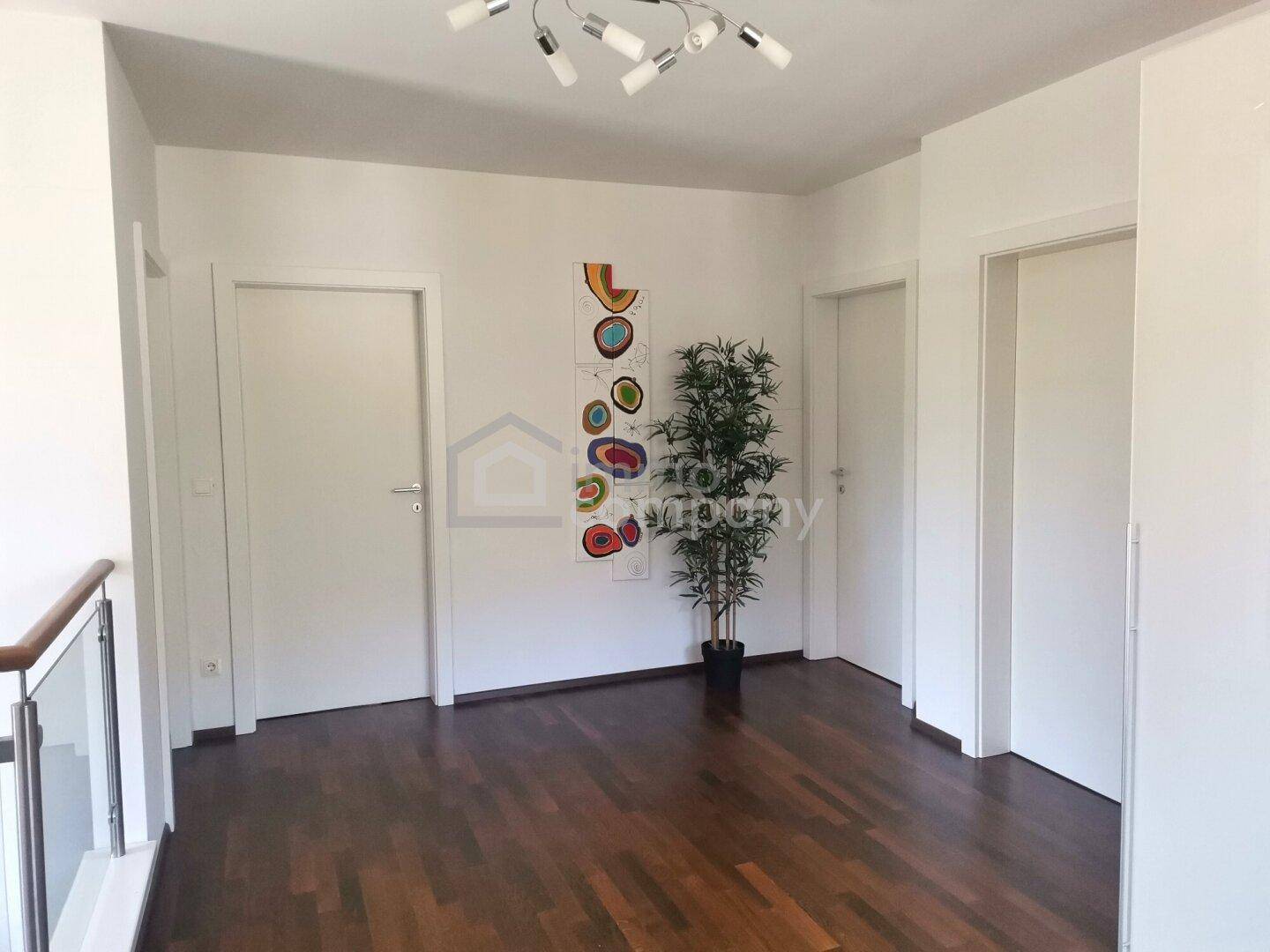 Heller Flur mit Holzboden und moderner Kunst an der Wand, der zu verschiedenen Räumen führt.