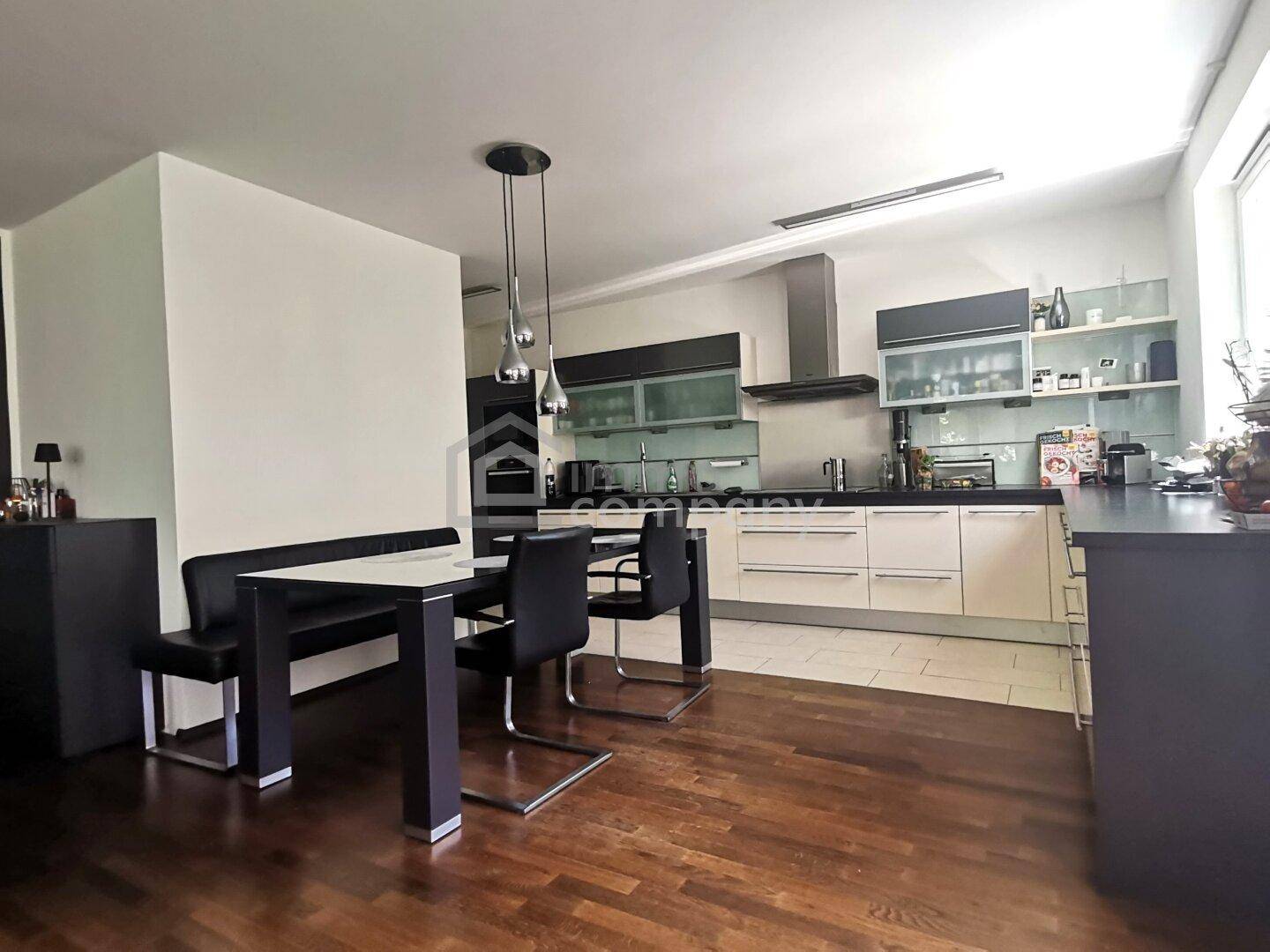 Moderne Einbauküche mit dunklen Arbeitsplatten und Essbereich mit Holzboden in offenem Design.