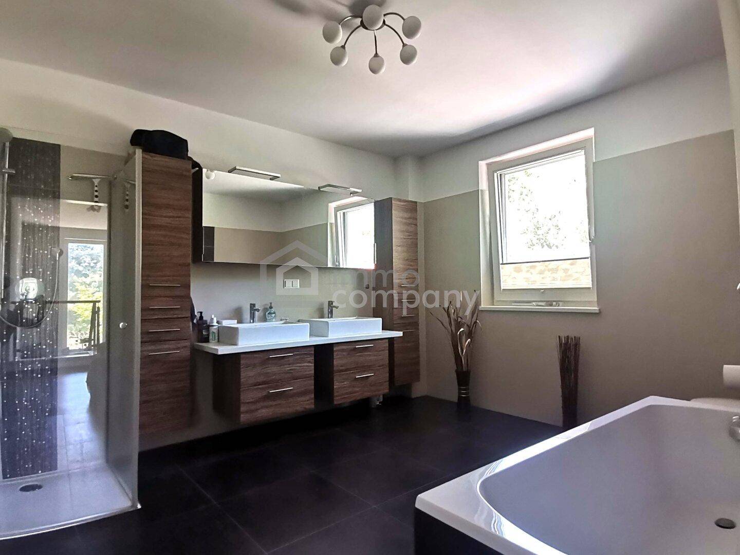 Geräumiges Badezimmer mit Doppelwaschbecken, Badewanne, Dusche und dunklen Fliesen.