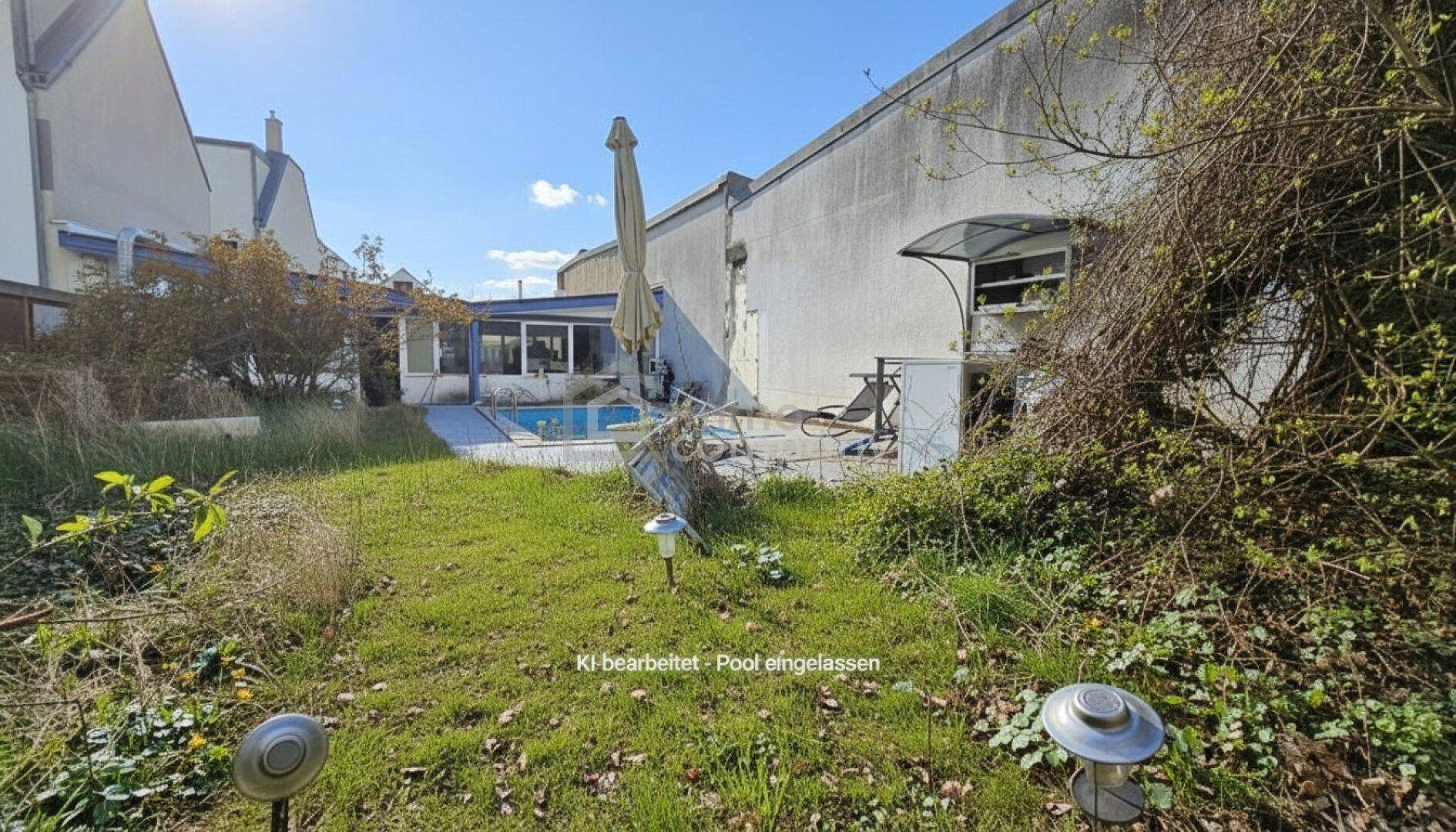 Blick auf den Garten mit üppigem Grün im Vordergrund und einem Poolbereich im Hintergrund unter blauem Himmel.