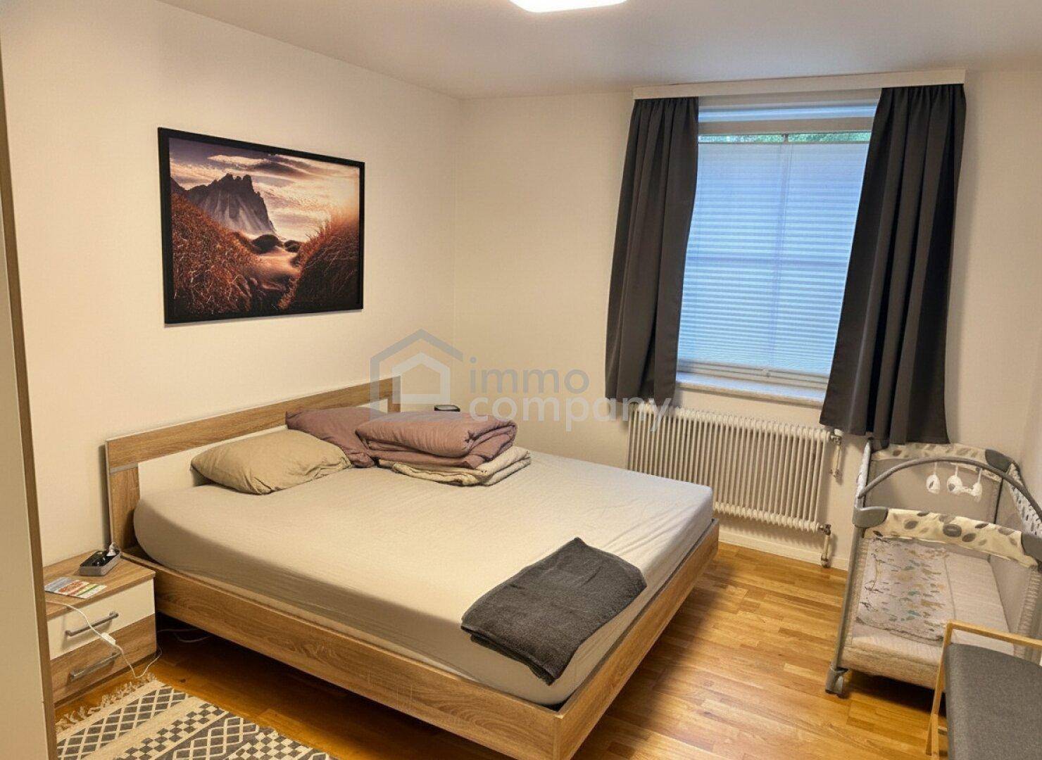Schlafzimmer mit Holzbett, Babybett und Fenster mit dunklen Vorhängen.