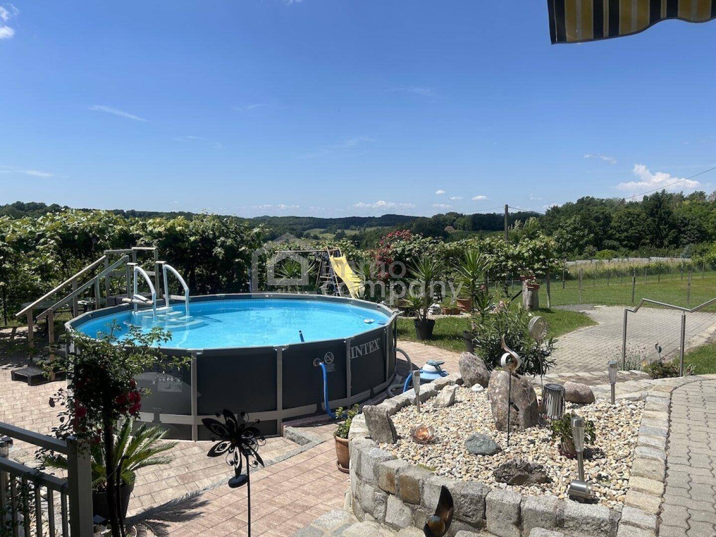 Weitläufiger Gartenbereich mit Aufstellpool, Rutsche und Panoramablick auf die umliegende Landschaft.