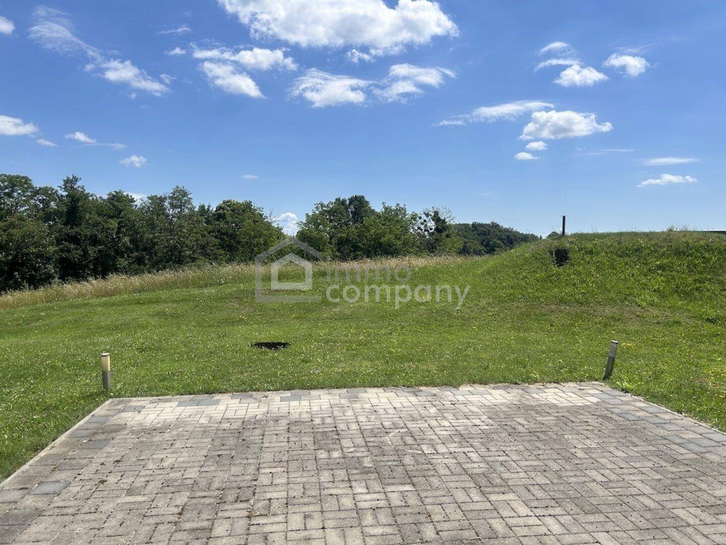 Gepflasterte Fläche in einer weiten grünen Landschaft unter einem klaren blauen Himmel.