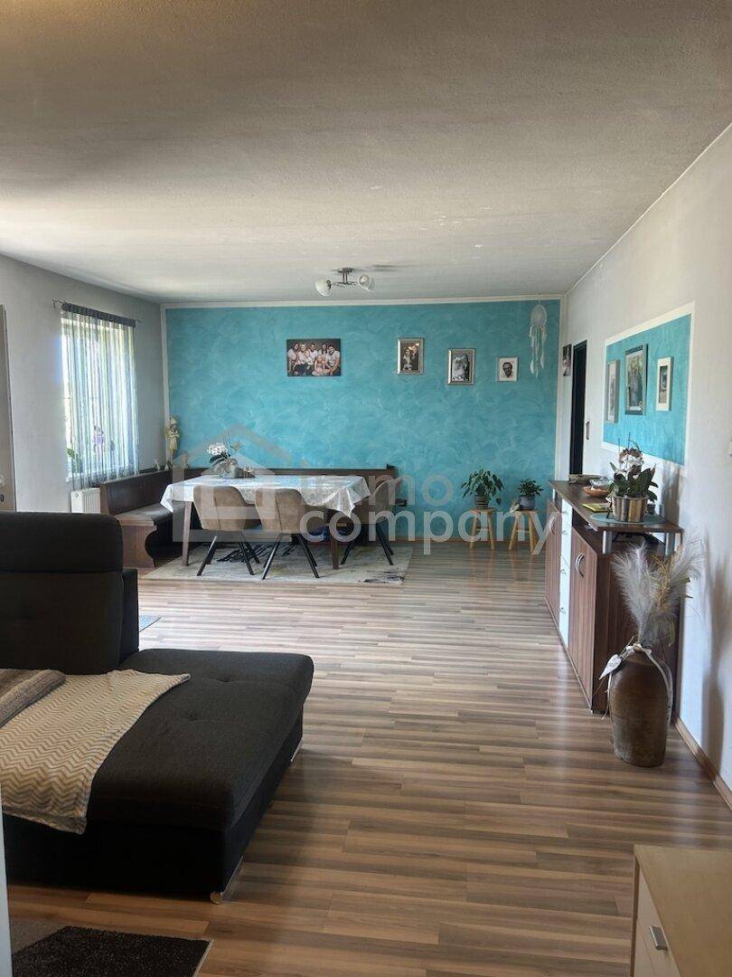 Geräumiger Wohn- und Essbereich mit Laminatboden, blauer Akzentwand und modernem Sofa.