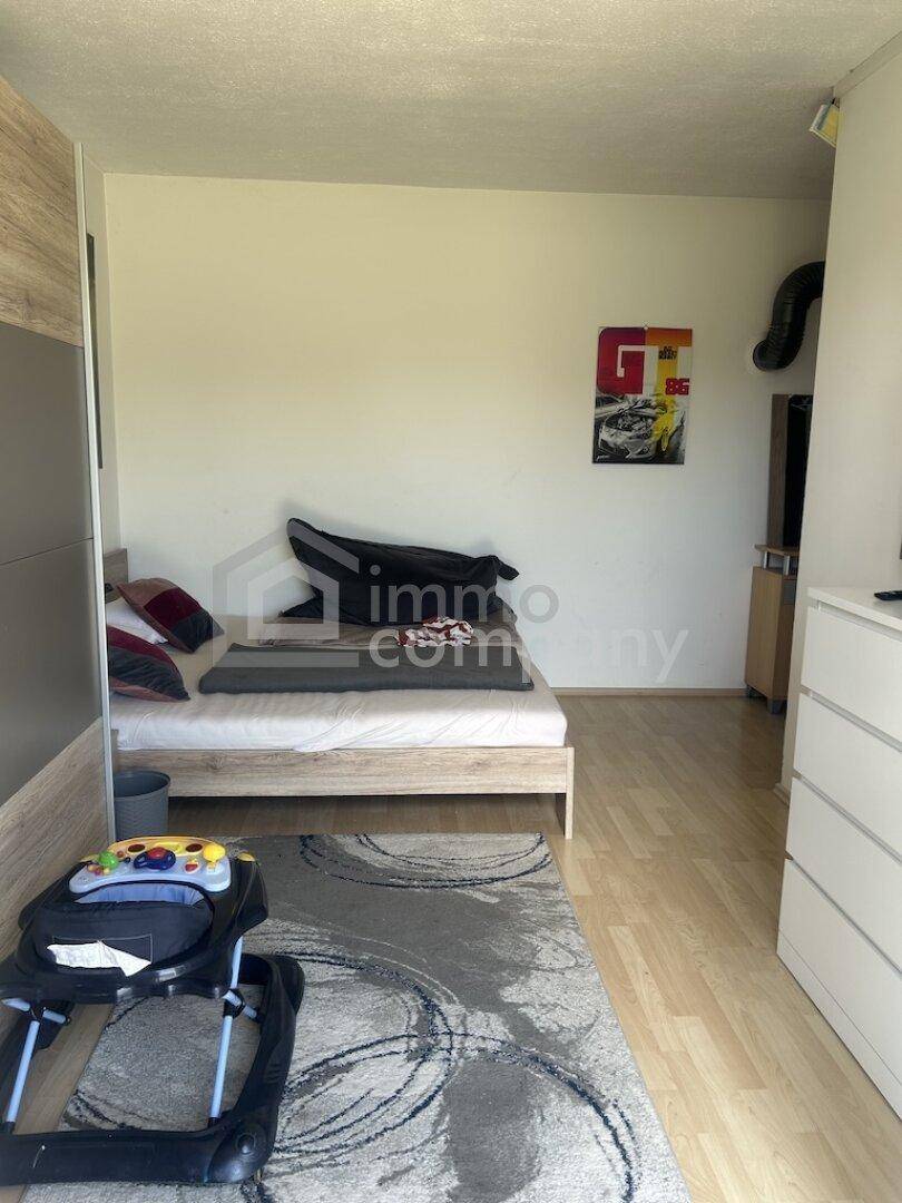 Schlafzimmer mit Laminatboden, hellem Bett und einem Kleiderschrank mit Holzoptik.