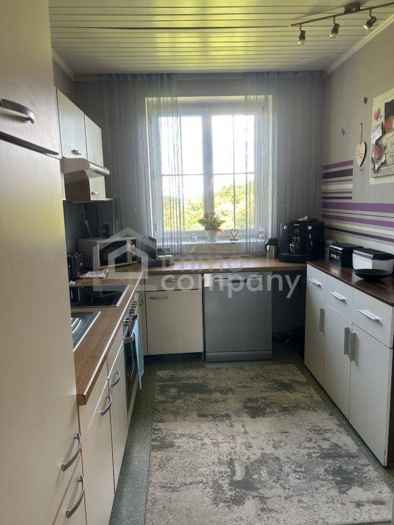 Funktionale Küche mit hellen Schränken, Arbeitsplatte in Holzoptik und Fenster mit Blick ins Grüne.