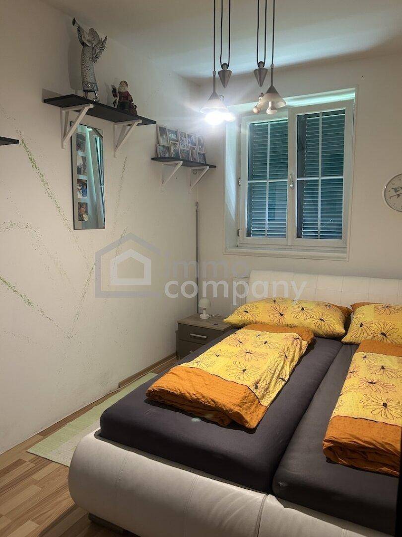 Schlafzimmer mit Doppelbett, Nachttischen und einem Fenster mit Jalousien für Privatsphäre.