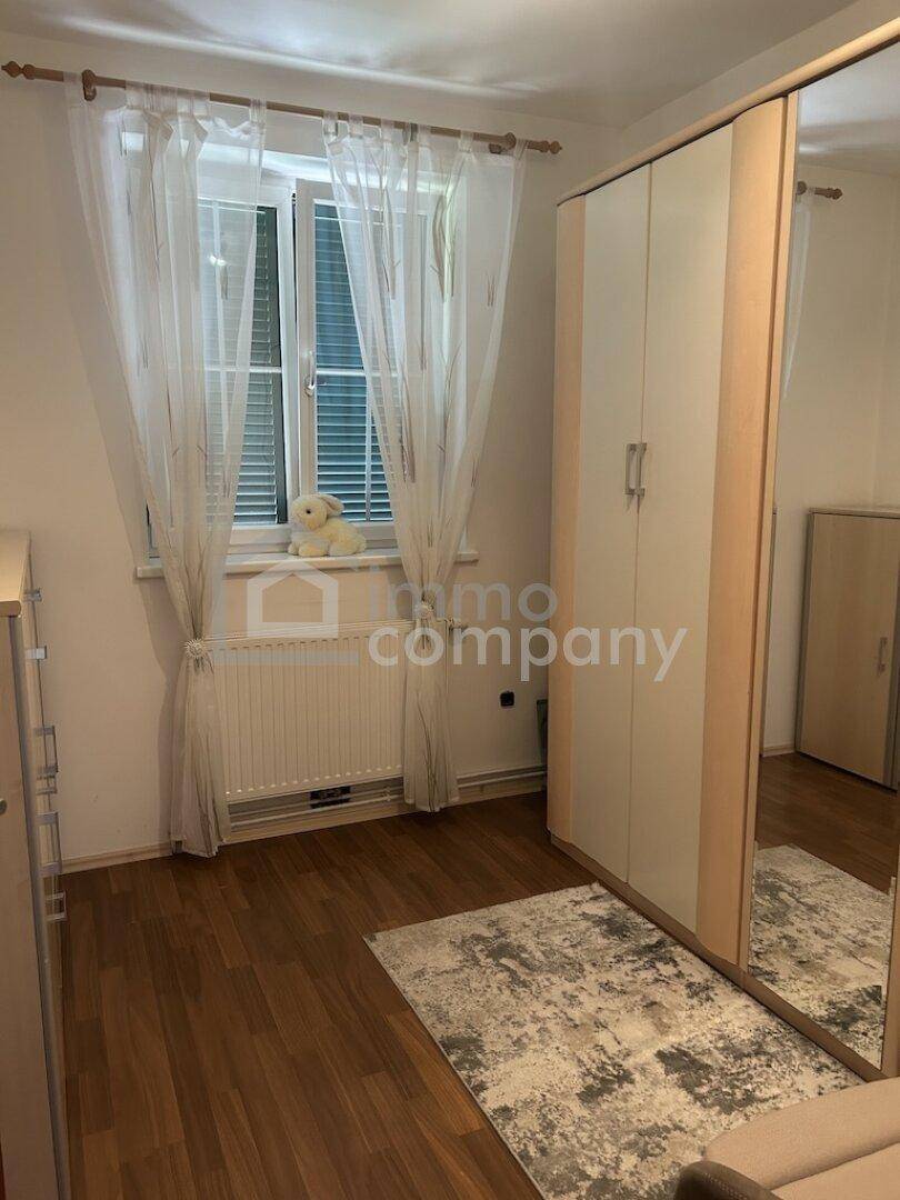 Helles Schlafzimmer mit Laminatboden, großem Spiegelschrank und Fenster mit Vorhängen.