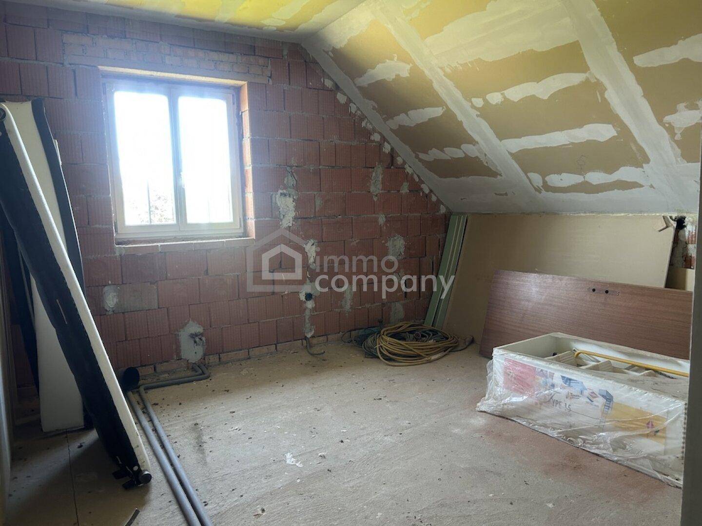 Unfertiger Dachbodenraum mit Ziegelwänden, schräger Decke und einem Fenster.