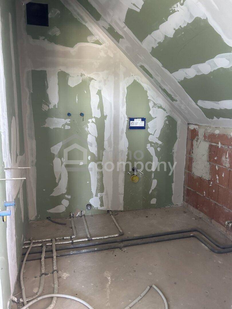 Unfertiges Badezimmer im Dachgeschoss mit vorbereiteten Anschlüssen und schräger Decke.