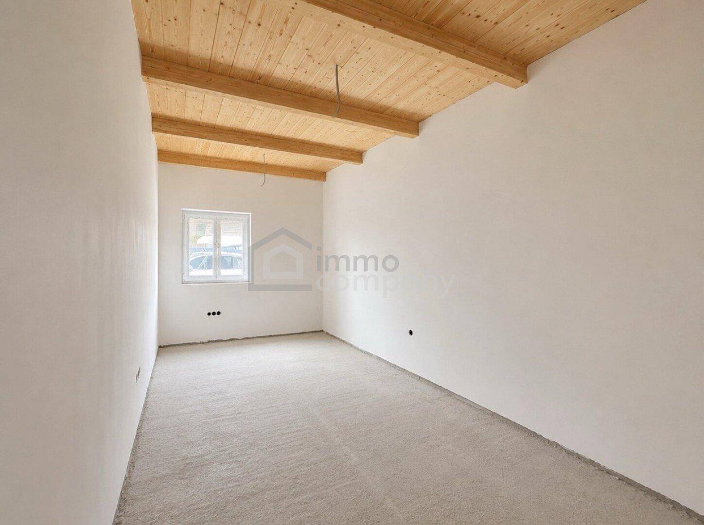 Helles Zimmer mit Holzbalkendecke und Fenster, bereit für individuelle Gestaltung.
