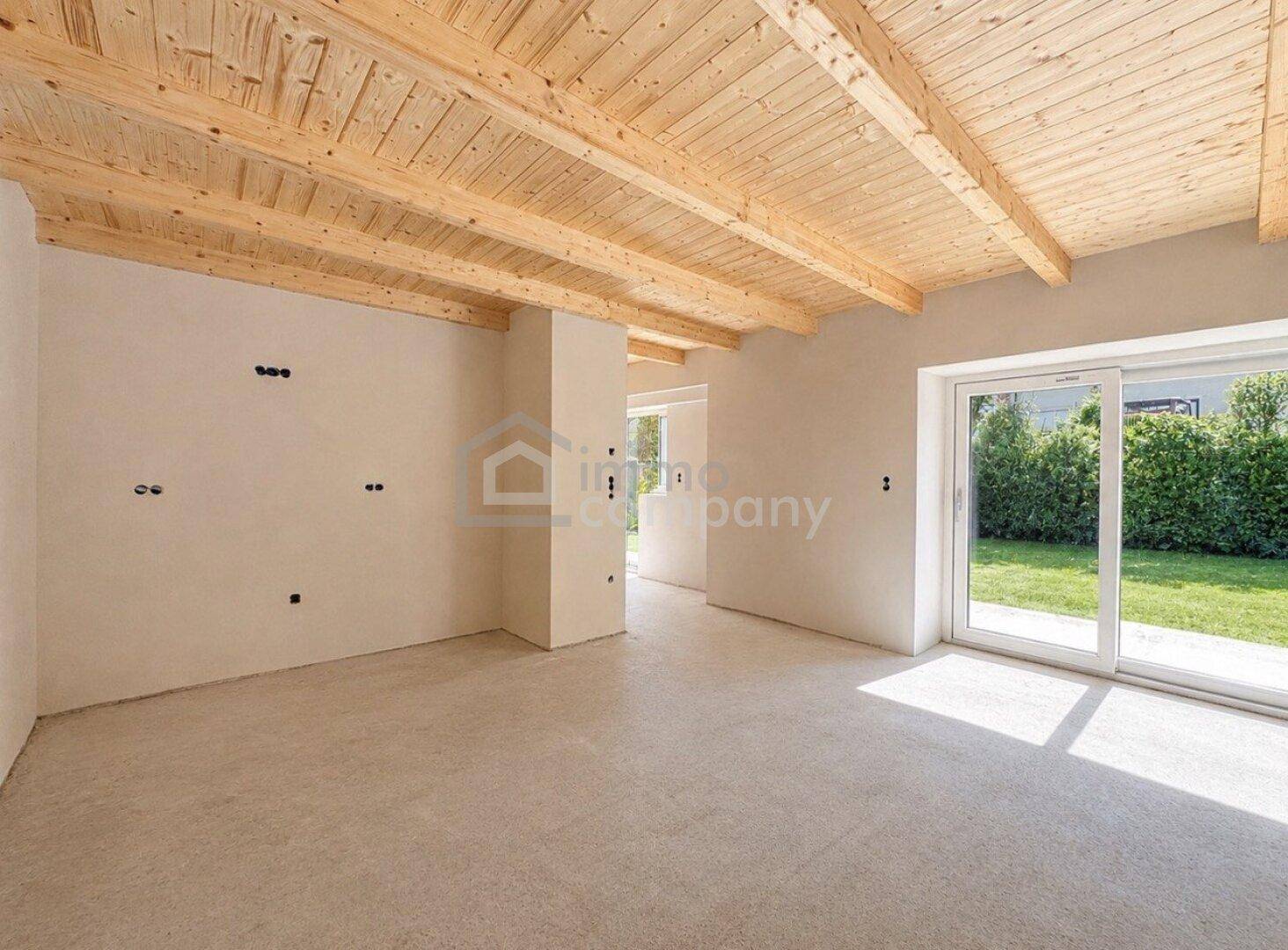 Geräumiger Wohnbereich mit Holzbalkendecke und viel Tageslicht durch die Terrassentür.