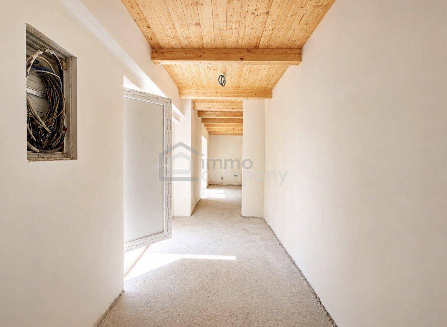 Langer Flur mit Holzbalkendecke und viel Tageslicht, noch im Bau.