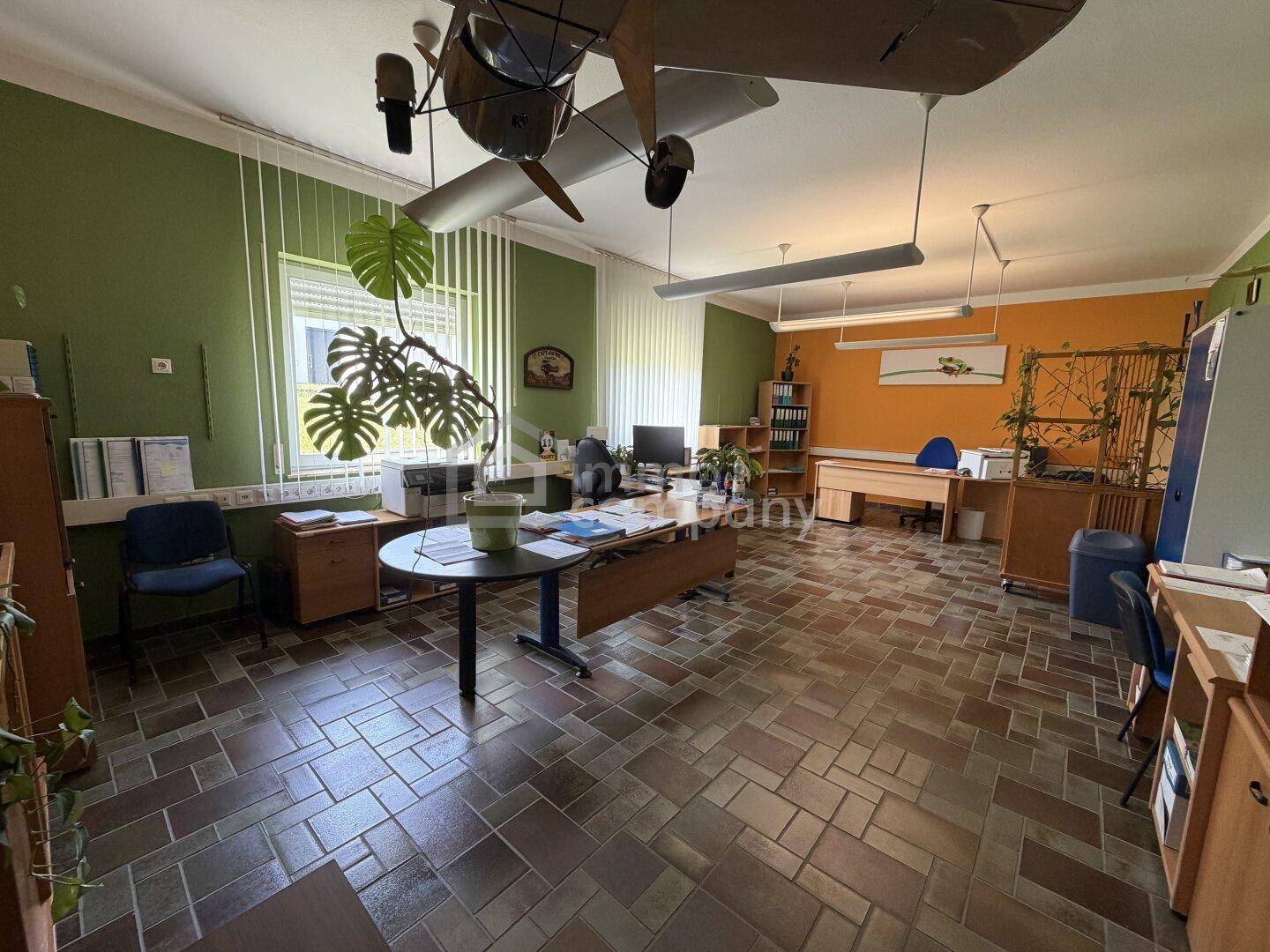 Geräumiges Büro mit mehreren Arbeitsplätzen, Fliesenboden und farbigen Wänden.