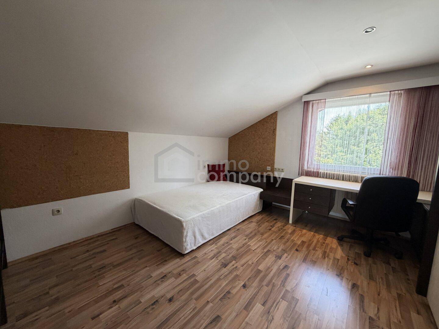 Schlafzimmer im Dachgeschoss mit Holzboden, Schreibtisch und schrägen Wänden.