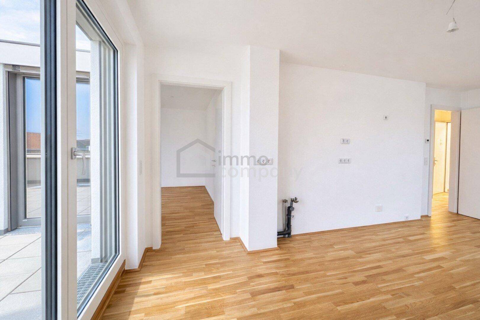 Heller Raum mit Holzboden und Zugang zu einer Terrasse, verbindet verschiedene Wohnbereiche.