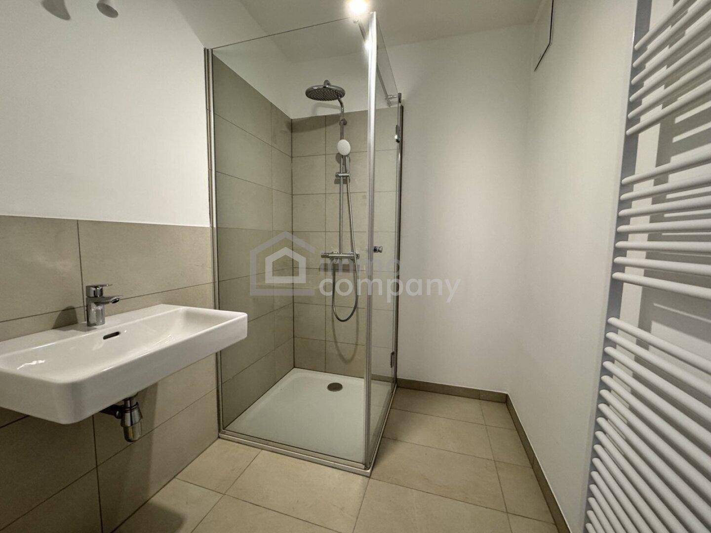 Modernes Badezimmer mit ebenerdiger Dusche, Einzelwaschbecken und beheiztem Handtuchhalter.