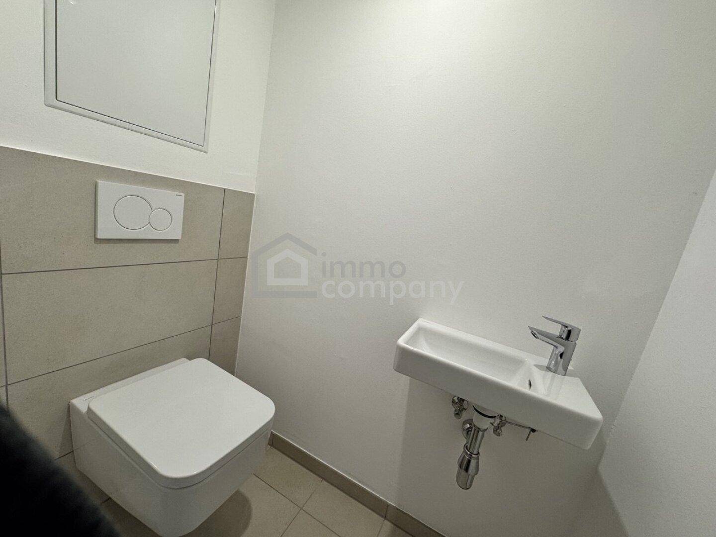 Kleines Gäste-WC mit wandhängender Toilette, modernem Waschbecken und hellen Fliesen.