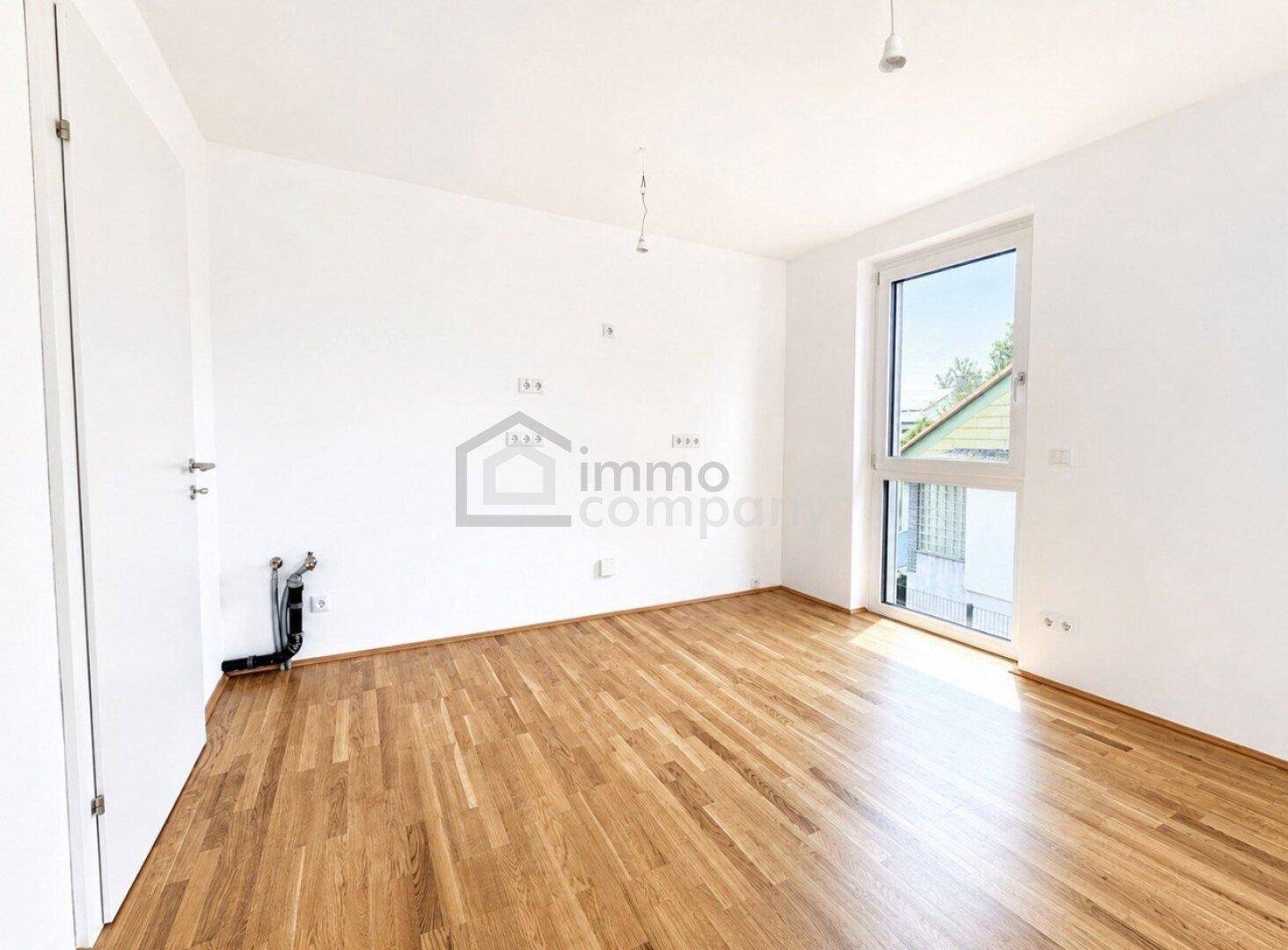 Leerer Raum mit Parkettboden, weiß gestrichenen Wänden und einem großen Fenster.