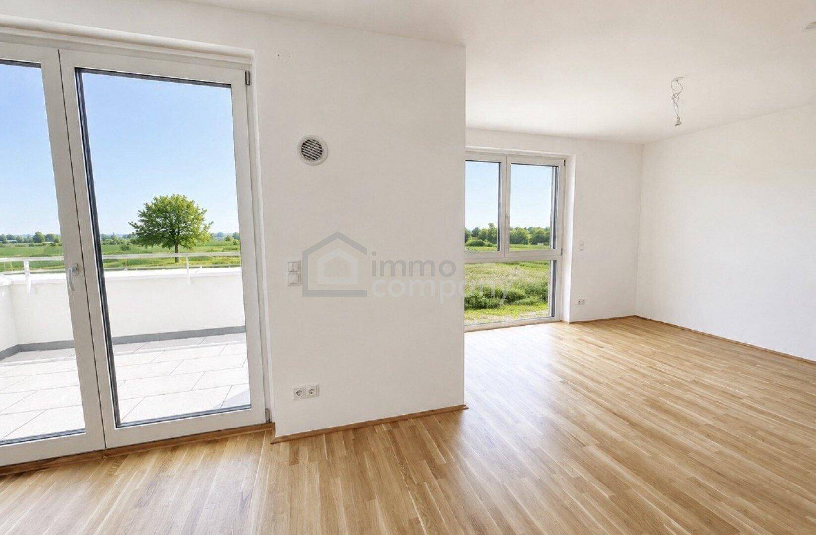 Lichtdurchfluteter Raum mit Holzparkett, großen Fenstern und Zugang zum Balkon mit freiem Blick ins Grüne.