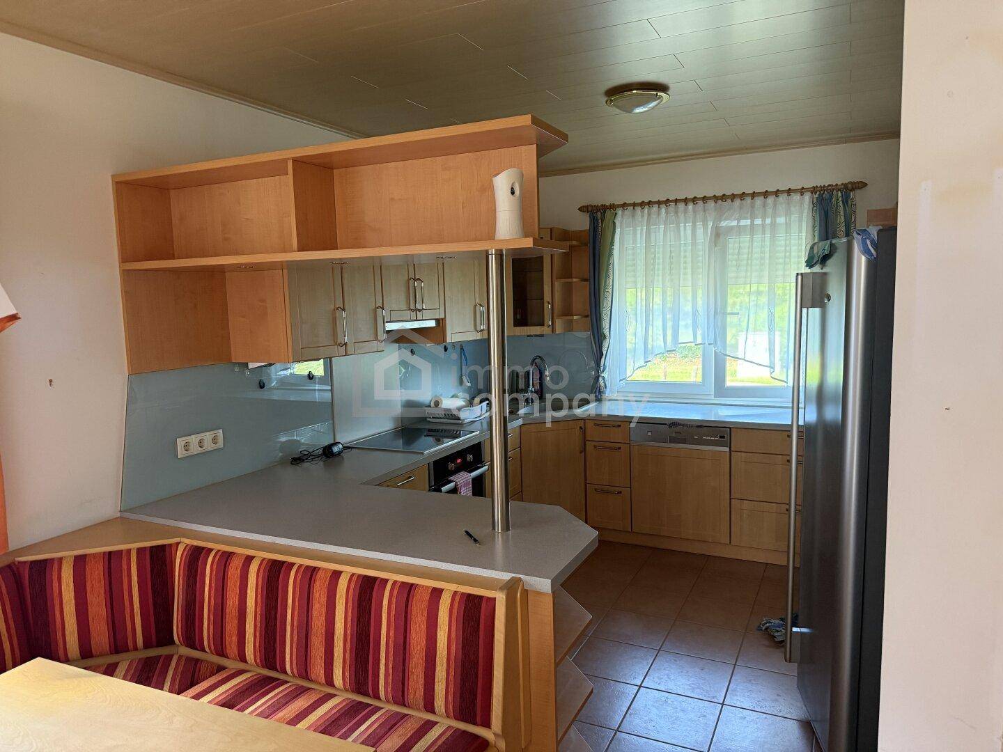 Funktionale Küche mit Holzeinbauten, Essbereich und Blick nach draußen.