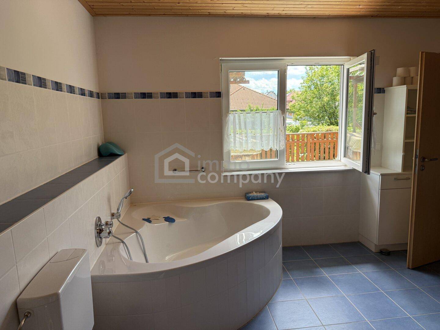 Badezimmer mit Eckbadewanne, blauen Fliesen und Fenster mit Blick ins Grüne.