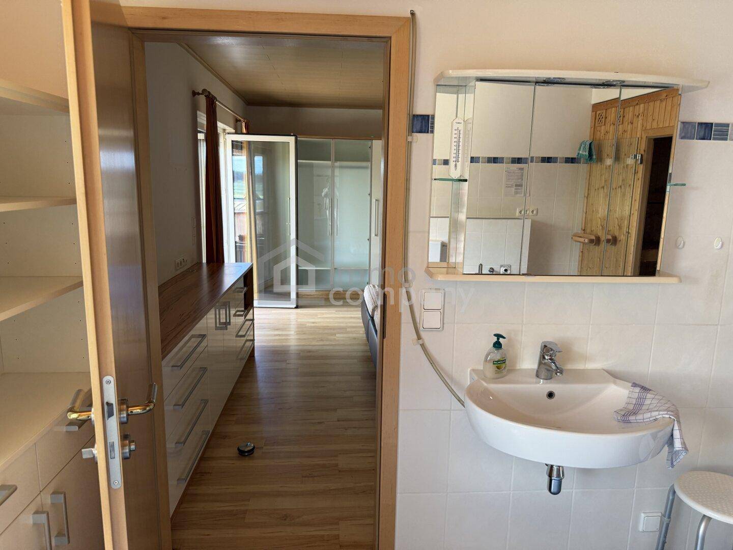 Badezimmer mit Waschbecken, Spiegelschrank und Blick in einen angrenzenden Raum.