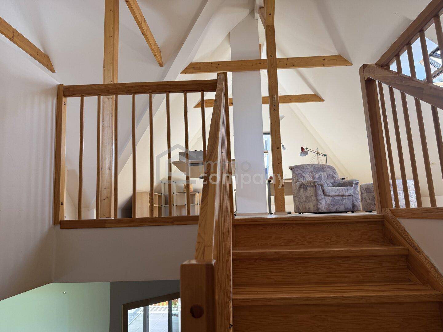Holztreppe führt zu einem offenen Dachbodenbereich mit sichtbaren Holzbalken.