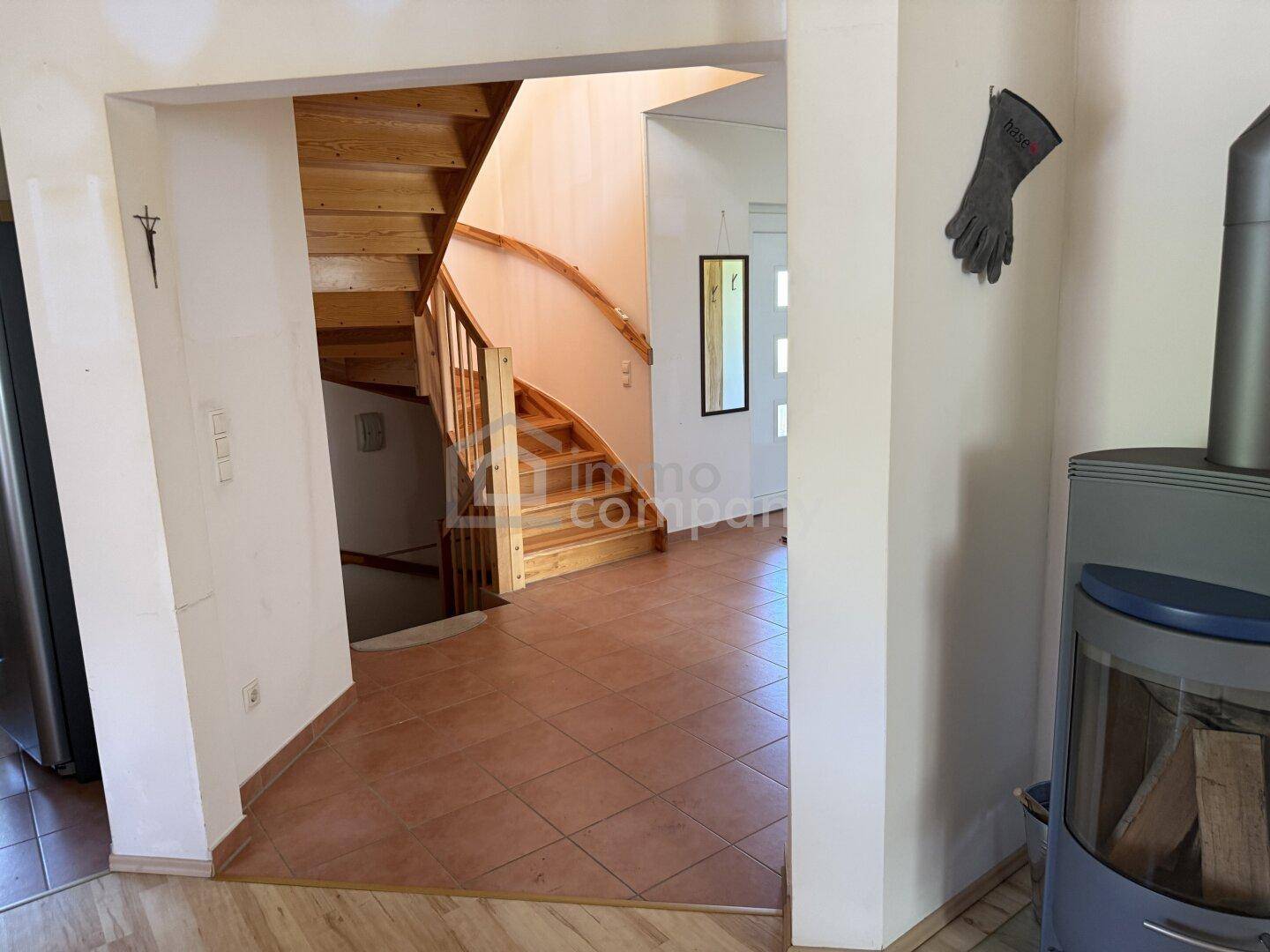 Eingangsbereich mit Fliesenboden, Holztreppe und Kaminofen im Hintergrund.